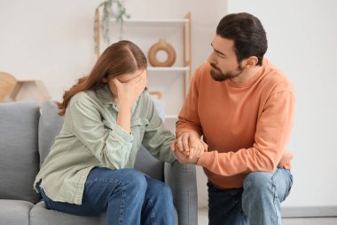 Evdeki kanepede üzgün karısından özür dileyen genç adam.