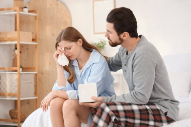 Elinde mendil kutusu olan genç bir adam yatak odasında ağlayan karısından özür diliyor.