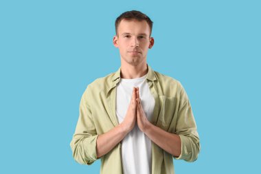 Mavi arka planda özür dileyen genç adam.