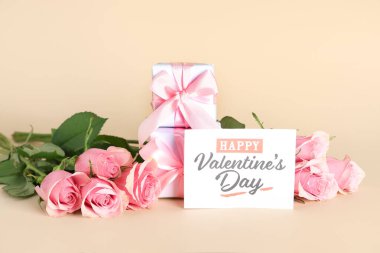 Gül çiçekli kompozisyon, hediye kutuları ve bej arka planda Mutlu Günler yazılı tebrik kartı. Sevgililer Günü kutlaması