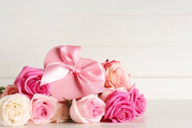 Beyaz ahşap arka planda gül çiçekleri ve kalp şeklinde hediye kutusu olan kompozisyon. Sevgililer Günü kutlaması