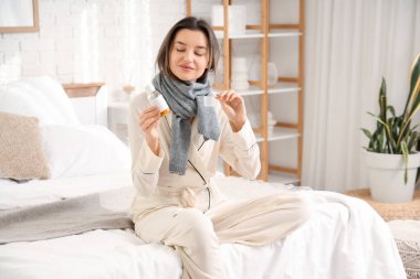 Yatak odasında öksürük şurubuyla oturan hasta genç bir kadın.