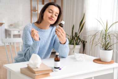 Yatak odasındaki masada öksürük şurubuyla hasta genç bir kadın.