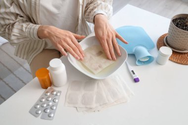 Young woman dipping mustard plaster into bowl of water in bedroom, closeup