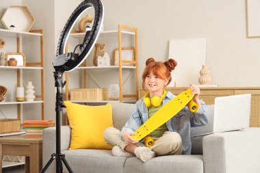 Evdeki kanepede kaykay yapan kızıl saçlı genç bir kız.