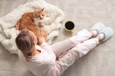 Pijamalı güzel bir kadın. Evde yumuşak terlikleri ve sevimli bir kedisi var.