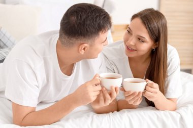 Yatak odasında kahve içen genç bir çift.