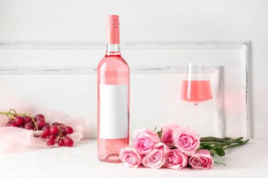 Beyaz arka planda güzel güller olan bir şişe ve bir bardak pembe şarap.