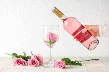 Pembe şarap şişesi ve beyaz fayans masasında güzel güller taşıyan kadın eli.