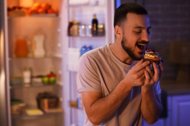 Geceleri mutfakta kek yiyen aç genç adam.