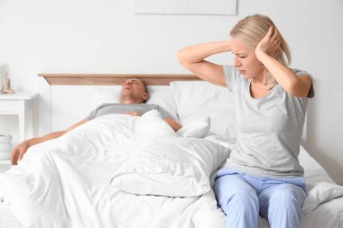 Kocası yatak odasında horladığı için kulaklarını tıkayan sinirli olgun bir kadın.