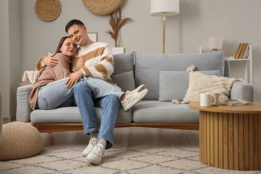 Evdeki kanepede sıcak kazaklar içinde kucaklaşan sevimli genç çift.