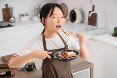 Genç Asyalı kadın mutfakta sebzeli tofu yiyor.