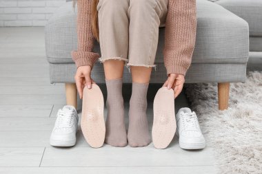 Ortopedik tabanlı ve spor ayakkabılı genç bir kadın evdeki kanepede oturuyor.