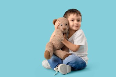 Sevimli küçük çocuk mavi arka planda oyuncak ayıya sarılıyor