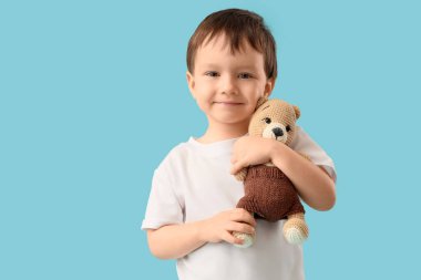 Sevimli küçük çocuk mavi arka planda oyuncak ayıya sarılıyor