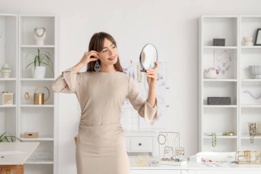 Atölyede küpe ve ayna takan genç bir bayan mücevher tasarımcısı.