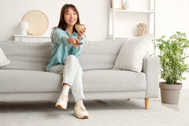 Kızarmış böcekli genç Asyalı kadın evdeki kanepede televizyon izliyor.