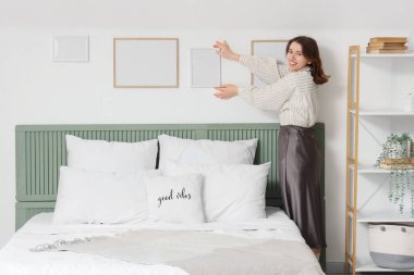 Young woman hanging blank frame on light wall in bedroom