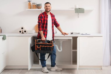 Mutfakta lavabonun yanında alet çantası olan erkek tesisatçı.