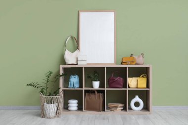 Şık çantalı raflar, boş çerçeve ve yeşil duvarın yanındaki bitkiler.