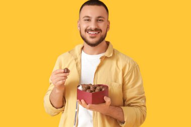 Sarı arka planda kalp şeklinde çikolata kutusu olan genç bir adam.