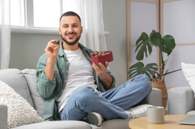 Evdeki kanepede oturan bir kutu çikolatalı genç adam.