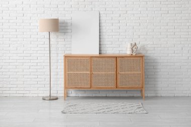 Odadaki beyaz tuğla duvarın yanındaki çekmecelerin üstündeki boş poster.