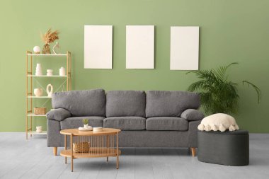 Rahat bir kanepe, sehpa ve yeşil duvarda boş posterler.