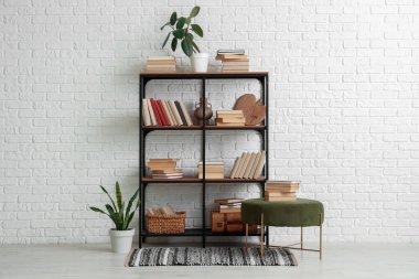 Rafa kaldırma ünitesi, kitap ve çiçeklerle dolu beyaz tuğla duvarın yanındaki oda.