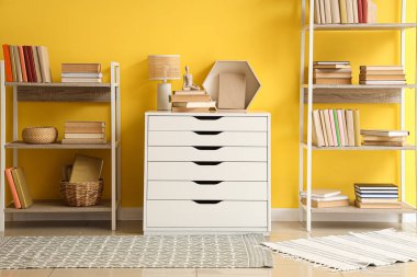 Çekmeceler ve raflar. Kitaplar sarı duvarın yanında.