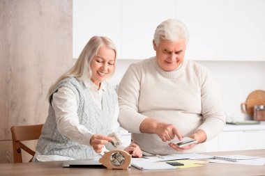 Kumbarası olan yaşlı çift mutfaktaki faturaları hesaplıyor.