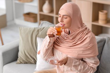 Genç Müslüman kadın evdeki kanepede Türk çayı içiyor.