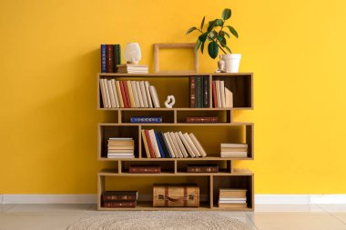 Sarı duvarın yanında lamba ve dekor olan bir kitaplık.