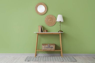 Yeşil duvarın yanındaki masada kitap bulunan şık bir lamba.