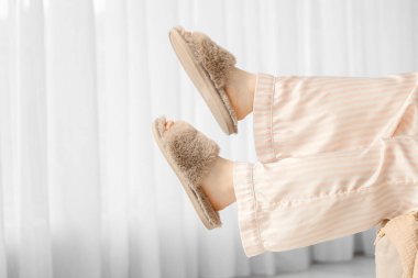 Evinin penceresinin yanındaki kahverengi terlikli genç kadın, yakın plan.