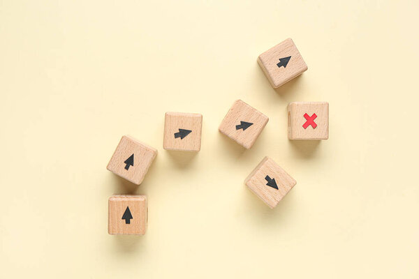 Wooden cubes with arrows and cross on beige background. Itinerary concept
