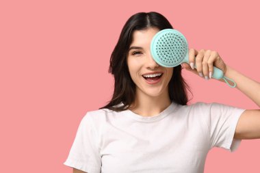 Pembe arka planda mavi saç fırçası olan güzel bir genç kadın.
