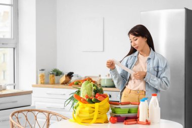 Genç Asyalı kadın mutfakta ürünleri kontrol ediyor.