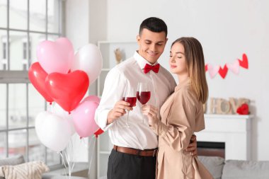 Kalp şeklinde balonları ve kadehleriyle evde sevgililer gününü kutlayan genç ve güzel bir çift.