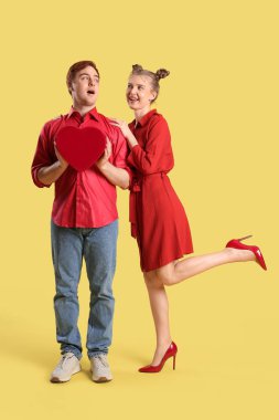 Sarı arka planda hediye kutusu olan genç bir çift. Sevgililer Günü kutlaması