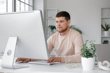 Genç sakallı adam evdeki masada bilgisayar kullanıyor.