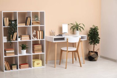 Çalışma odası ve bej duvarın yanında kitaplığı olan modern oturma odasının içinde.