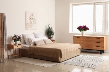 Büyük yataklı bir yatak odası ve çekmeceli bir vazoda leylak çiçekleri.