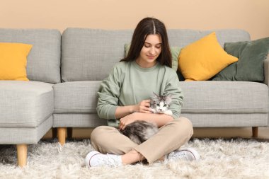 Uzun saçlı tatlı kedisi olan genç bir kadın oturma odasında yerde oturuyor.