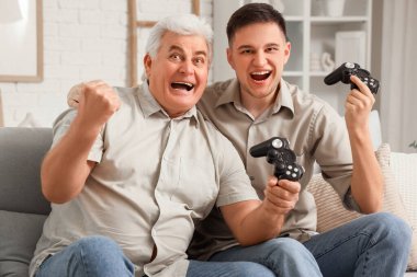 Babasıyla evdeki kanepede video oyunu oynayan mutlu genç bir adam.