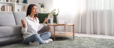 Genç Asyalı kadın oturma odasında meditasyon yapıyor.