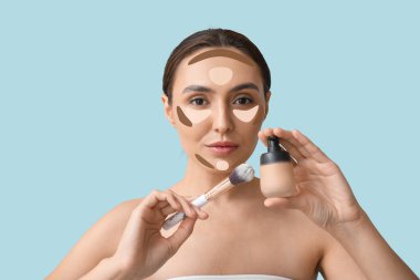 Güzel genç bir kadın açık mavi arka planda makyaj yapıyor.