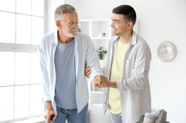 Genç adam babasının eve yürümesine yardım ediyor.