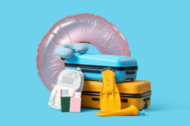 Seyahat yastığı, palet ve mavi arka planda şişme yüzük olan bavullar. Seyahat kavramı
